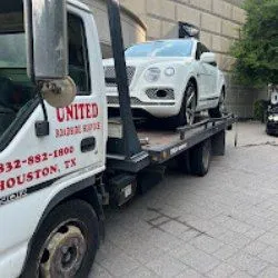 A white Bentley SUV is safely transported on a United Roadside Service flatbed tow truck, ensuring secure loading, careful handling, reliable transportation, premium towing, and dependable roadside assistance throughout Houston.