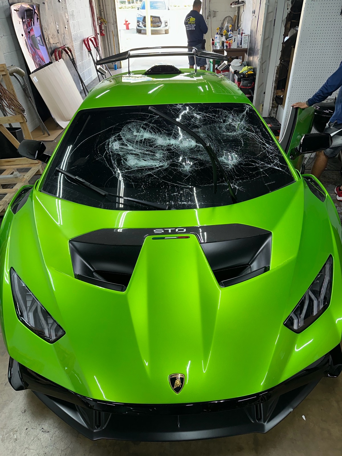 A green Lamborghini STO is shown with extensive cracks covering much of the windshield before replacement. The damage illustrates a situation requiring complete professional windshield replacement.