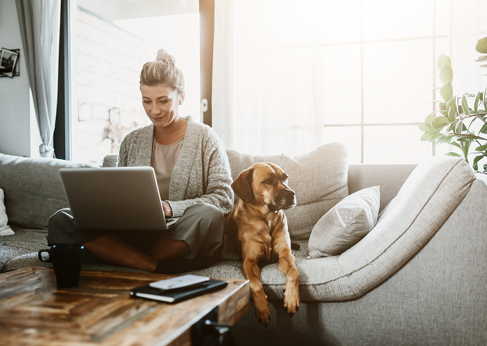 A woman on her laptop with her dog sitting next to her.