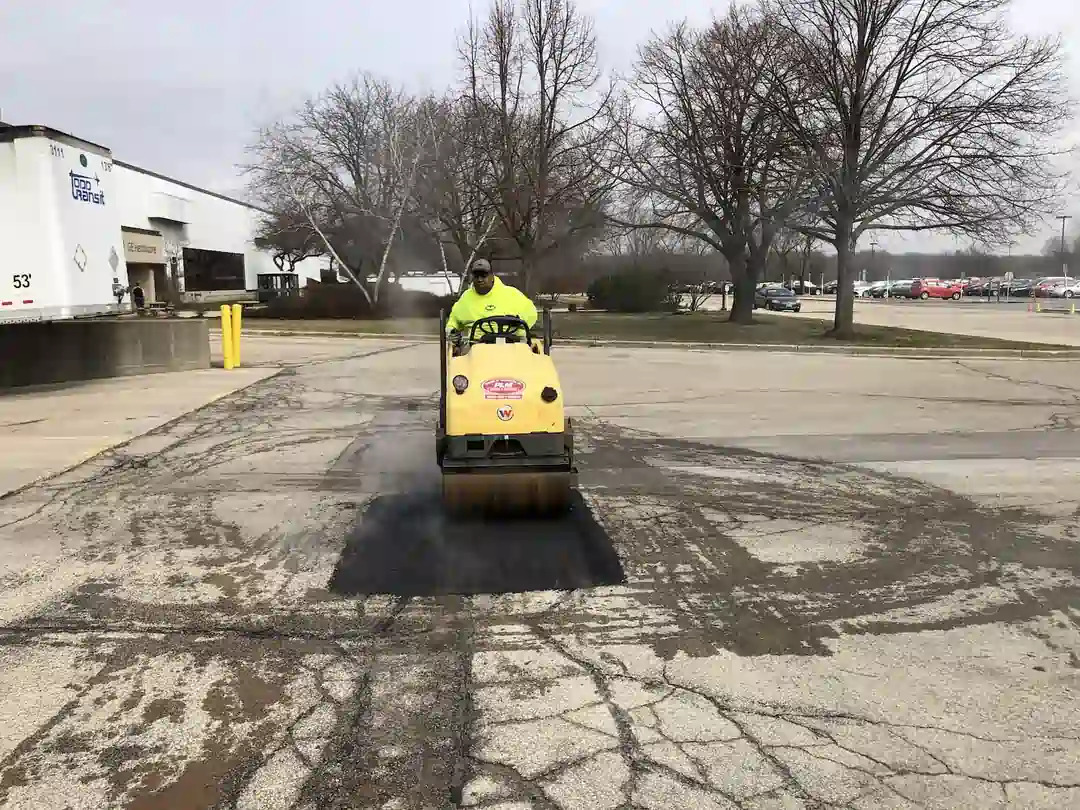 PLM crew member using a roller to perform asphalt patching.