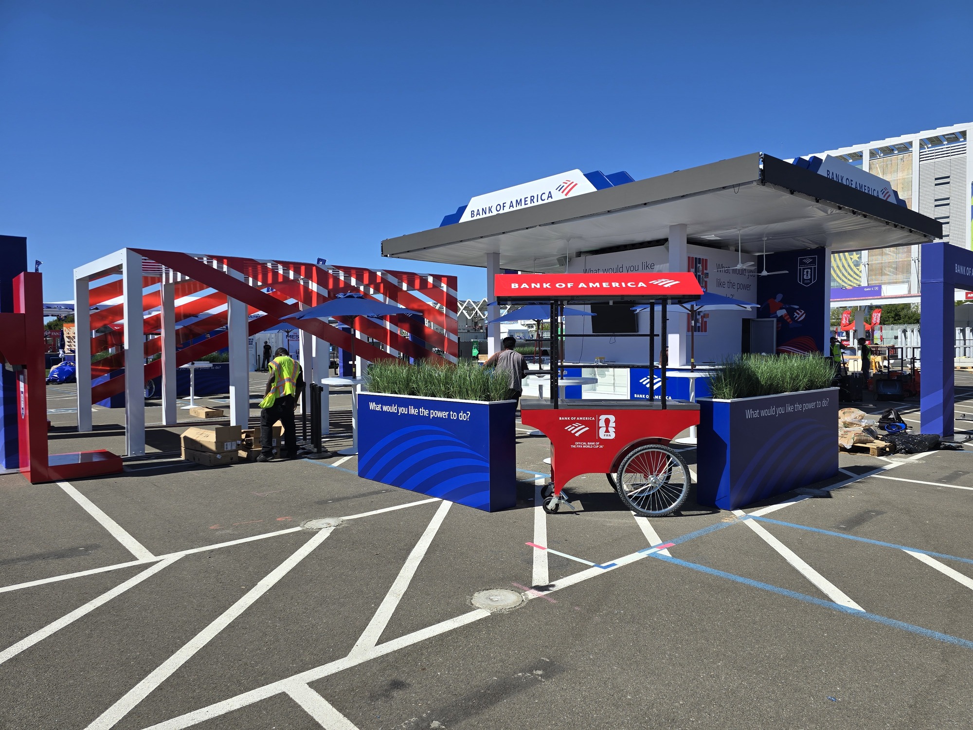 Wide view of the custom Bank of America outdoor brand activation featuring a FIFA World Cup event cart, branded planter walls, hospitality areas, and red, white, and blue exhibit structures.