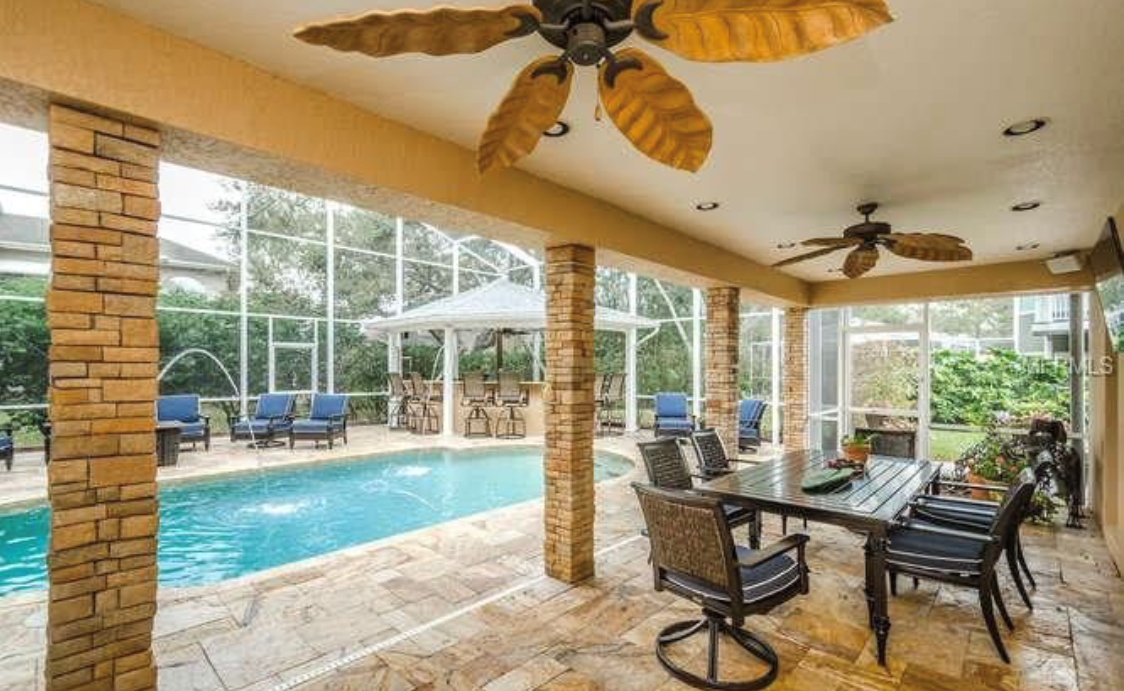 Screen-enclosed backyard swimming pool with a covered outdoor living area, stone columns, patio furniture, and ceiling fans.