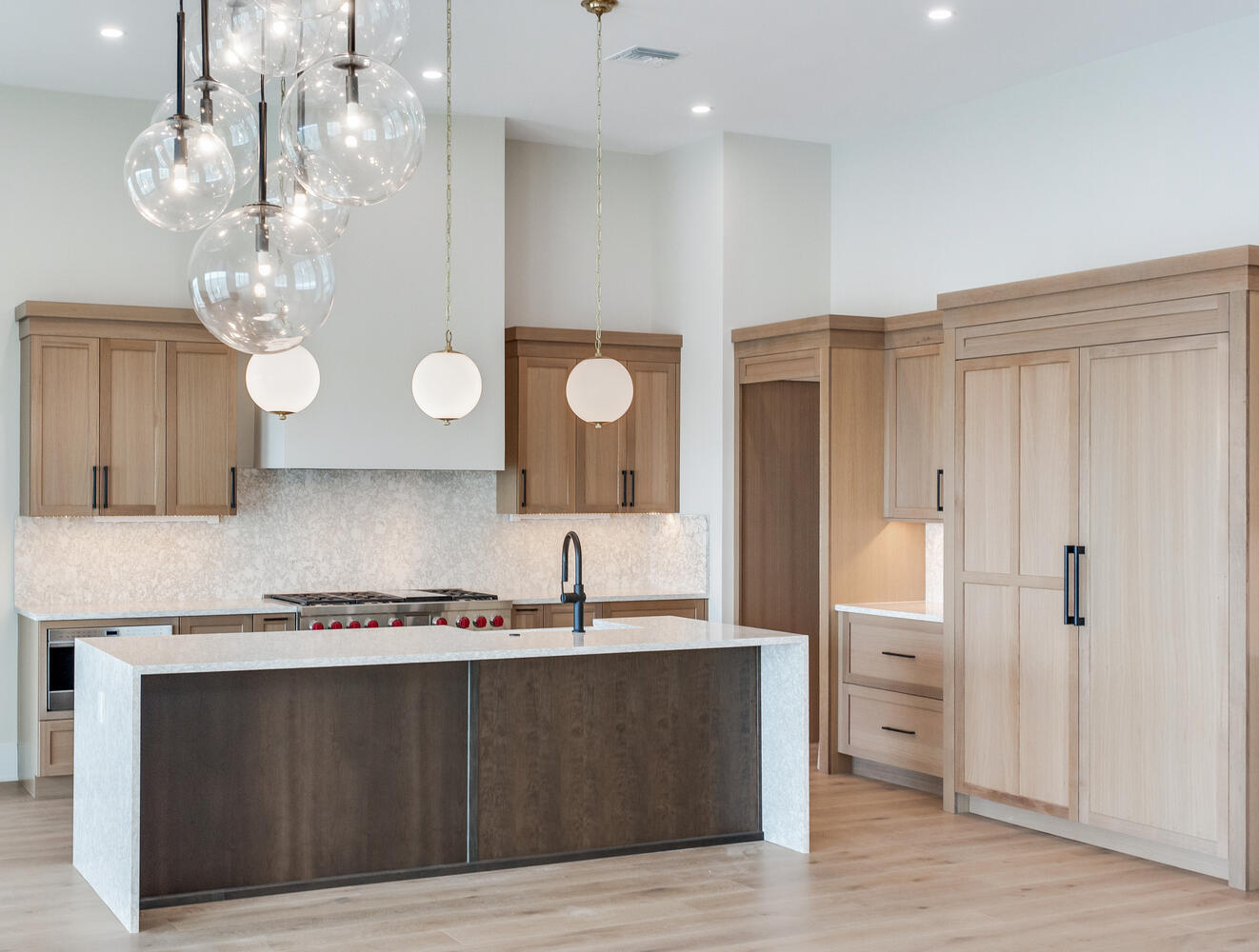 Luxury AVENTIS kitchen featuring a large waterfall island, custom wood cabinetry, statement pendant lighting, built-in appliances, and elegant modern finishes.