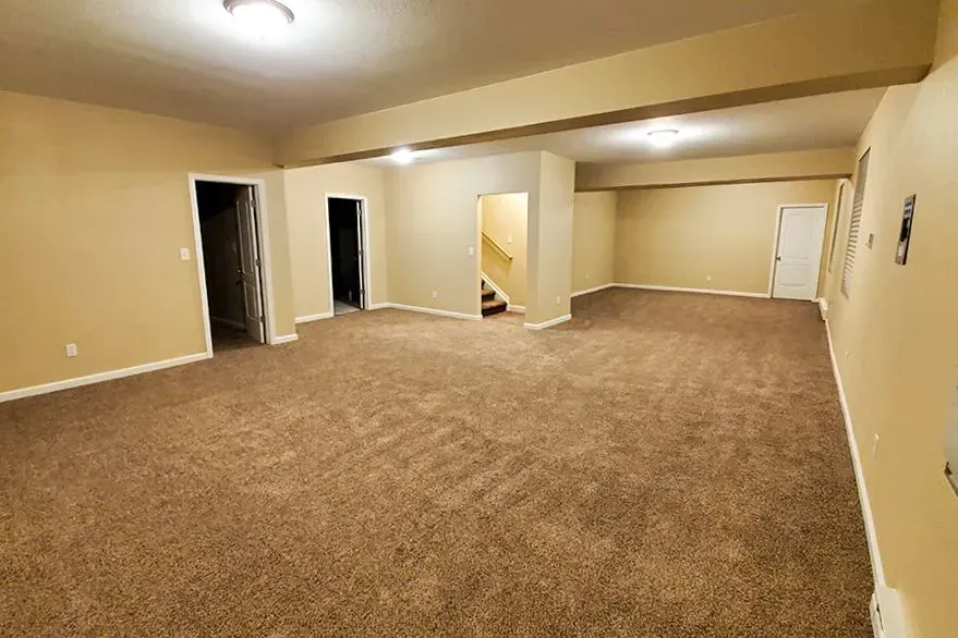 Expansive basement space with carpet flooring, support columns, multiple room entrances, and staircase access, providing excellent potential for future finishing, recreation, or additional living areas.