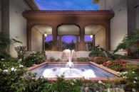 Dusk view of courtyard with fountain, beautiful flower landscaping, and archway with stairs.