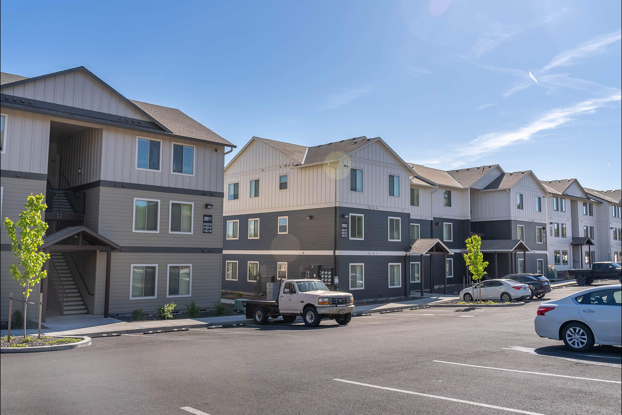 A row of modern townhouses with cars parked in front.