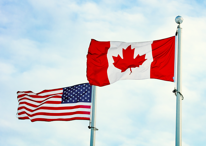 An American flag and Canadian flag flying side by side against a blue sky.