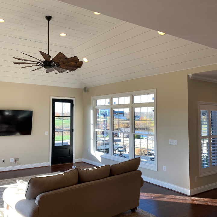 Fee Construction LLC delivered this stunning living room renovation in Evansville, IN featuring a white shiplap vaulted ceiling, statement ceiling fan, hardwood floors, and large picture windows with water views. From additions to full interior renovations, Fee Construction transforms spaces throughout Evansville and the tri-state area. Call (812) 626-1013 or visit feeconstruction.com to get started.