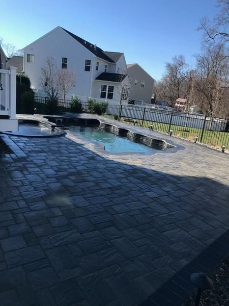 Spacious backyard with swimming pool and extensive paved patio area. The clean layout, fencing, and surrounding homes highlight professional hardscape installation, creating a functional outdoor space designed for leisure, gatherings, and long-term durability.