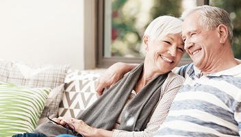 A retired couple smiling together while relaxing on their couch.
