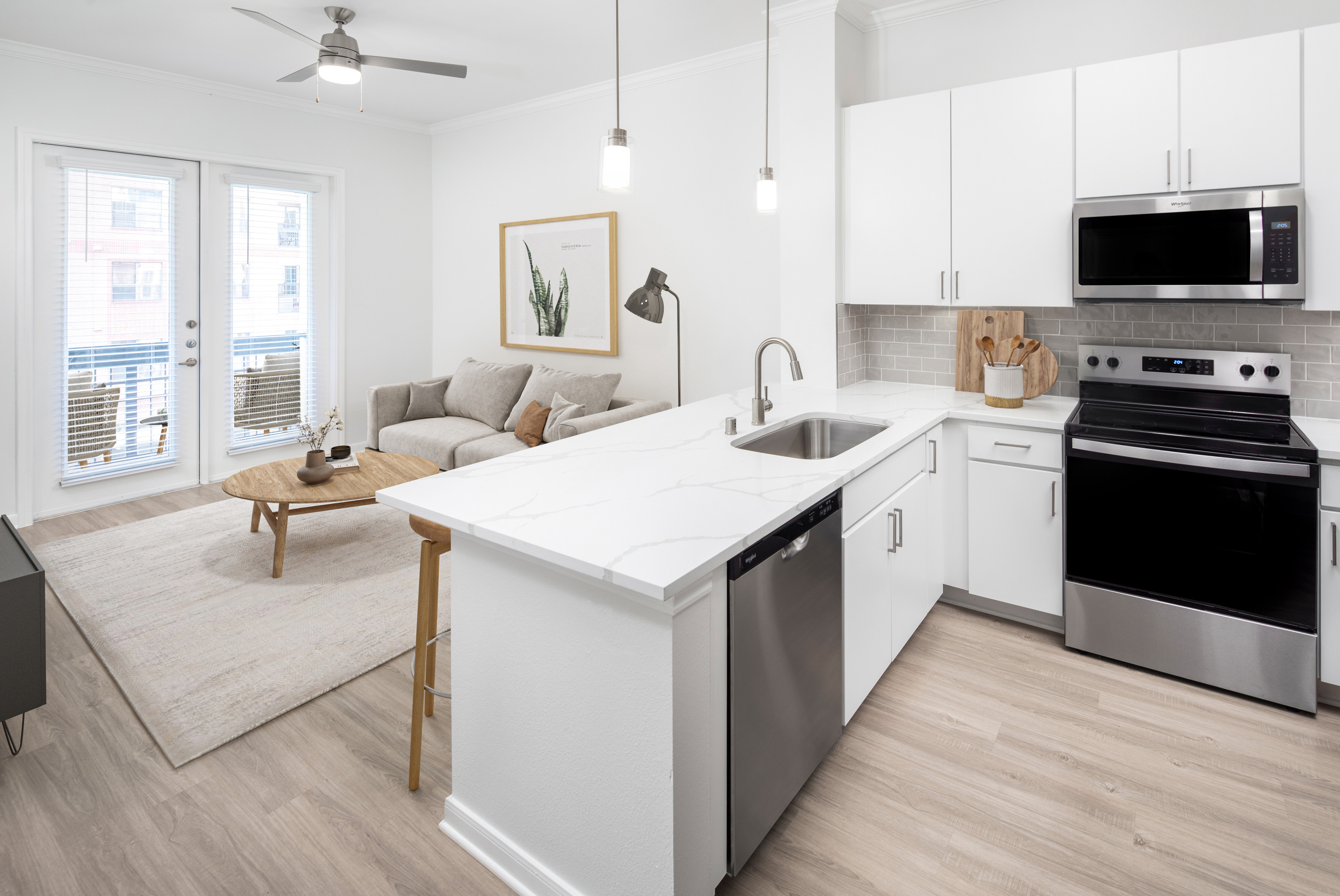 Modern kitchen and living room with white cabinetry, grey subway tile backsplash, white quartz counter tops with grey veining and stainless steel appliances at Camden Travis Street in Midtown Houston, Tx