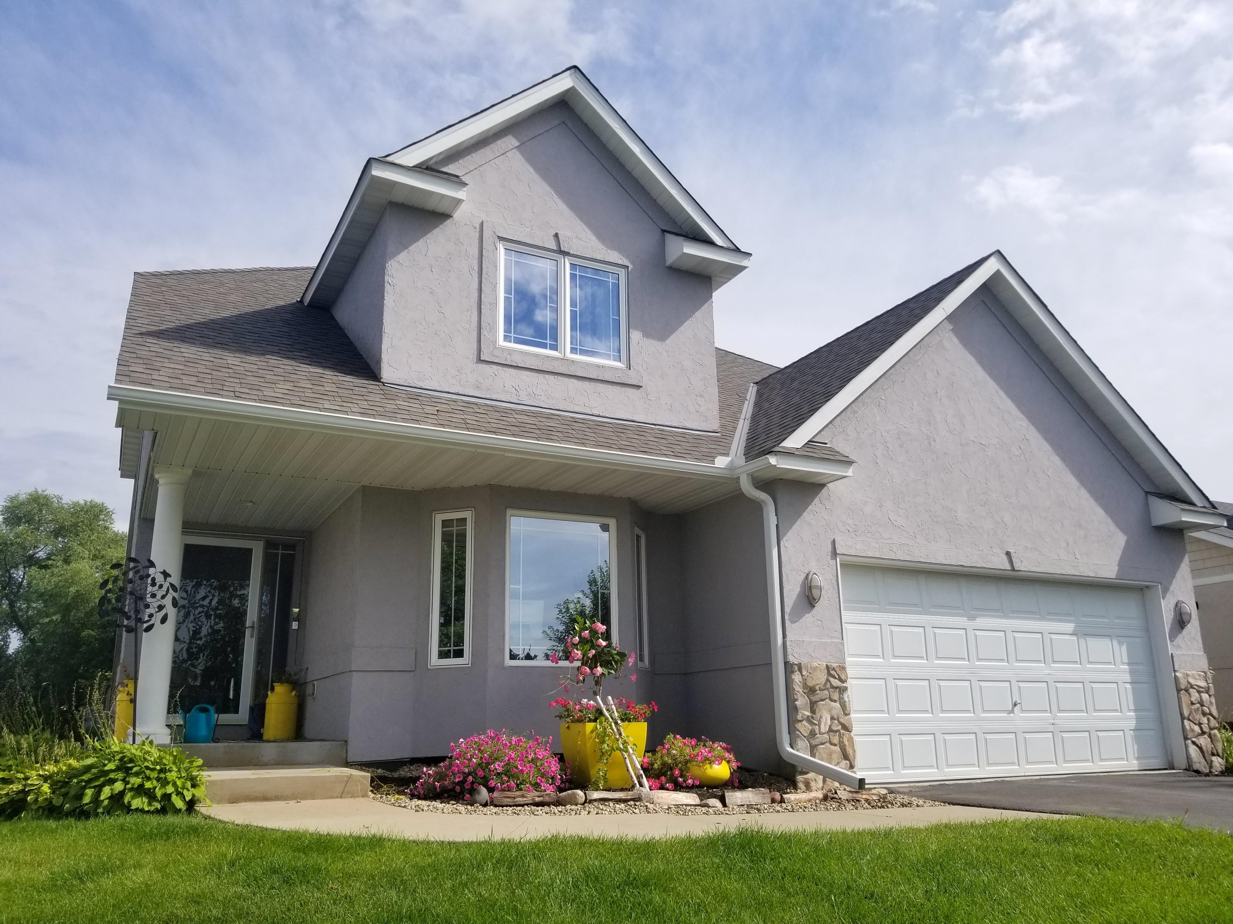 Clean white seamless gutters and downspouts installed on a beautiful two-story grey stucco home by Ultimate Gutter Solutions.
