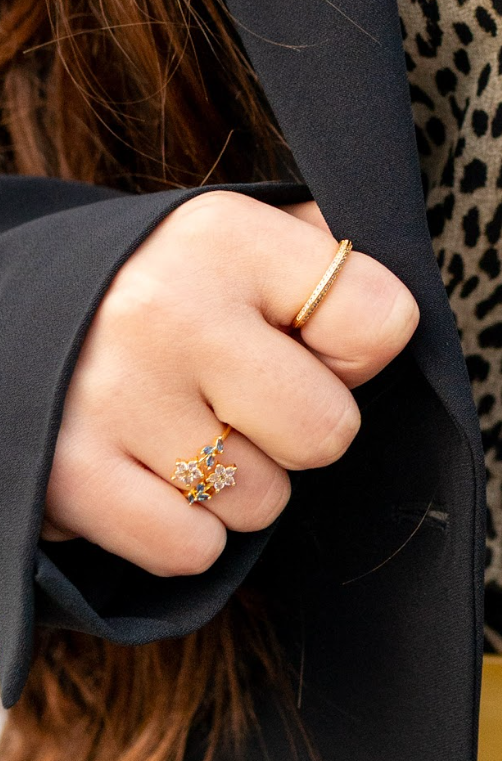Gold-toned rings featuring a floral design with blue accents and a slim sparkling band complement a black blazer. Discover elegant jewelry at Eliana Curated in Old Town Alexandria, VA, for daily wear.