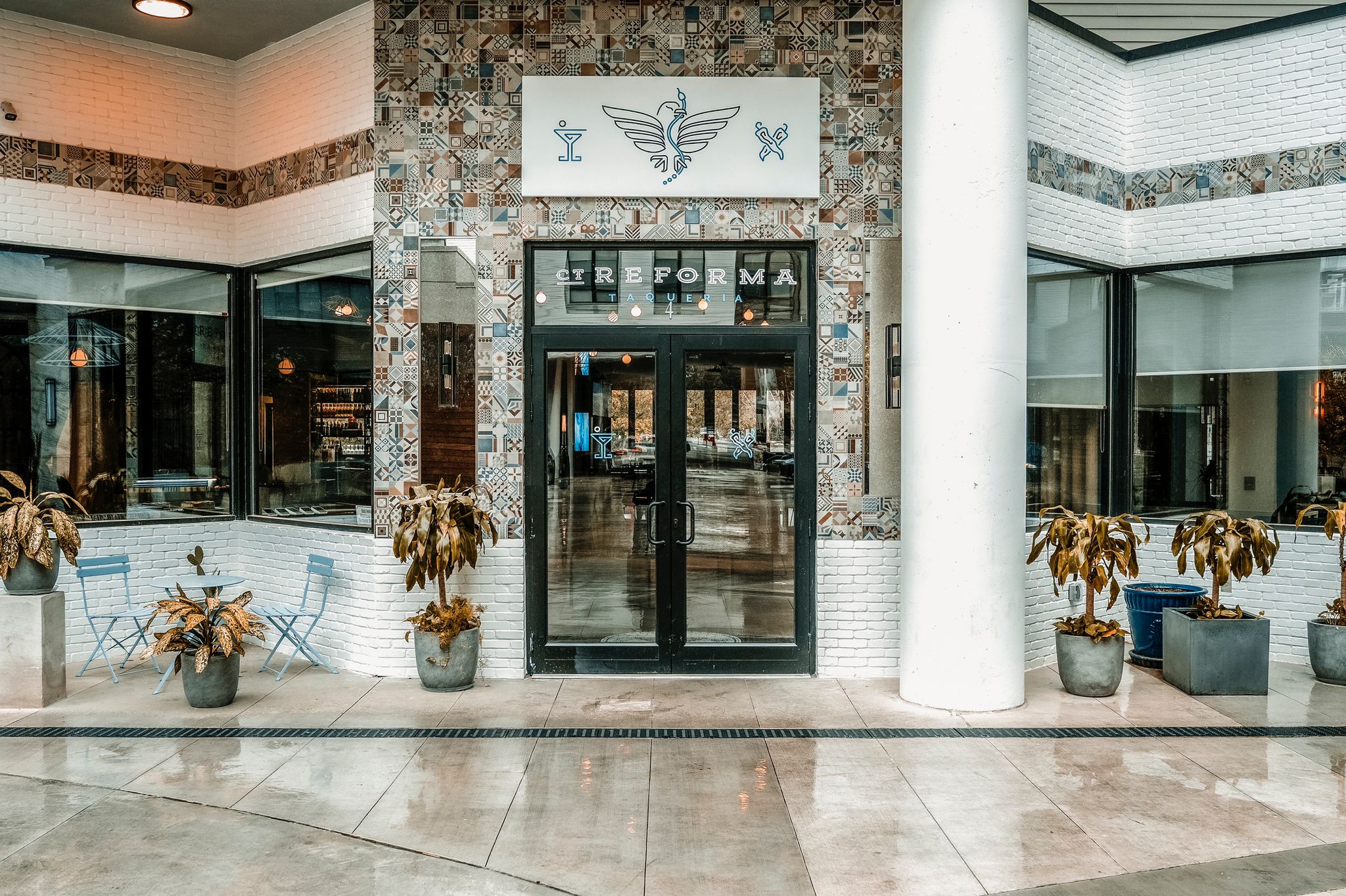 he entrance features a bold design with tall columns creating an elegant frame. The decorative tiles surrounding the door reflect a Mexican-inspired aesthetic, while the patio setup adds a casual yet refined vibe.