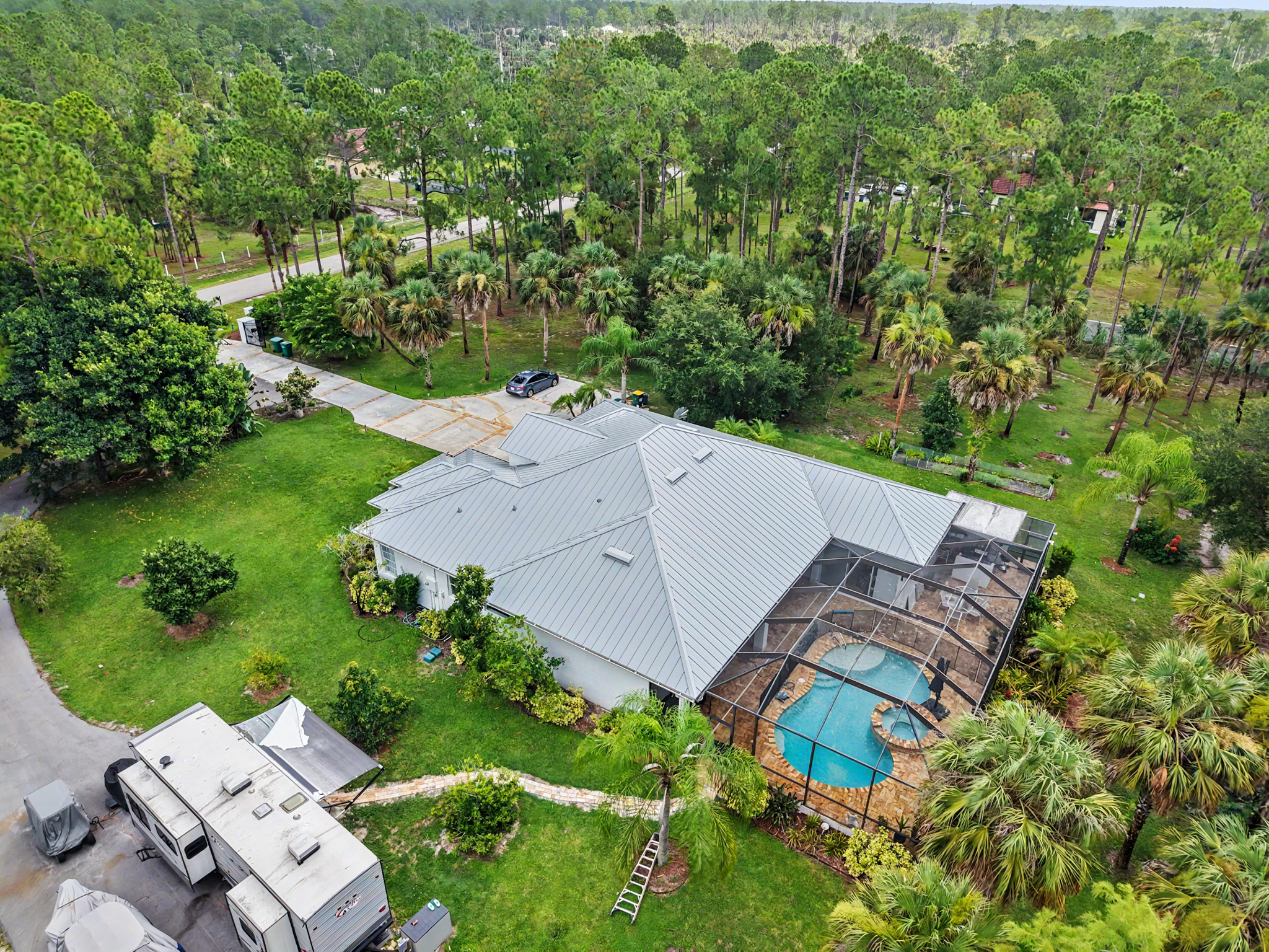 Wide aerial view of a residential property with a light gray metal roof, screened swimming pool, and 