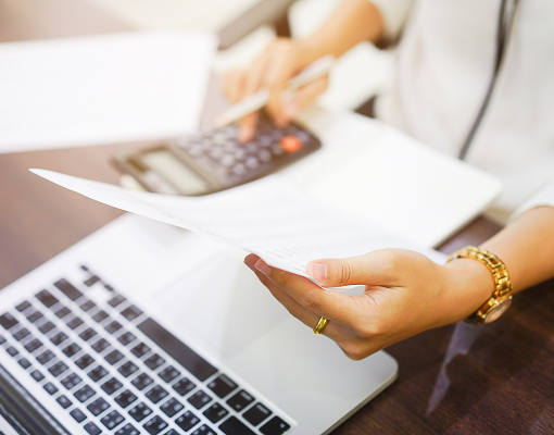 A person reviewing a document while typing on a calculator.