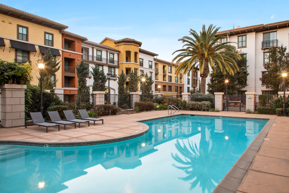 Pool with lounge seating, luxury landscaping, and view to Tuscan-inspired property exterior.