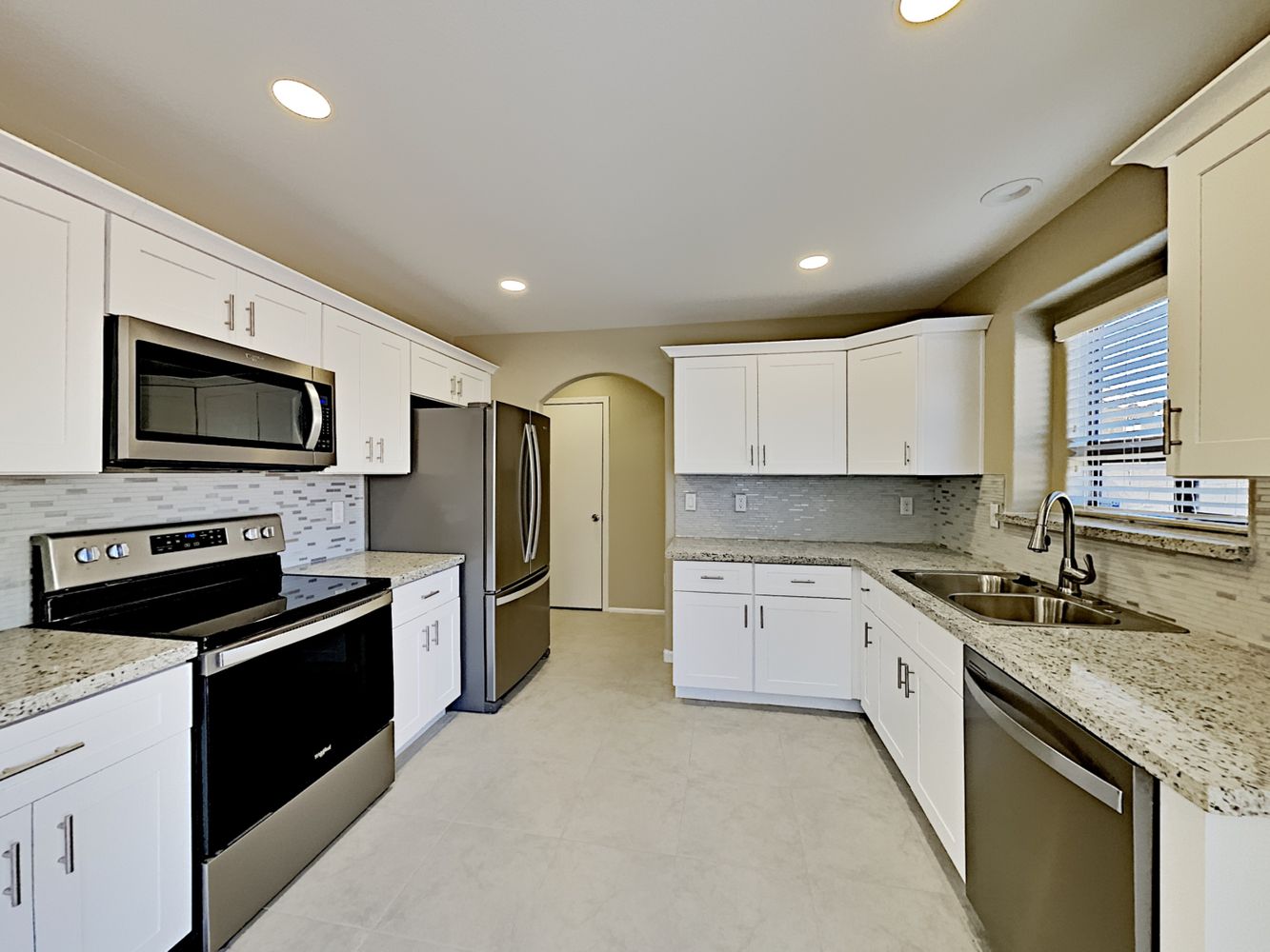 Modern kitchen with granite countertops, stainless-steel appliances, white cabinets and recessed lighting at Invitation Homes Phoenix.