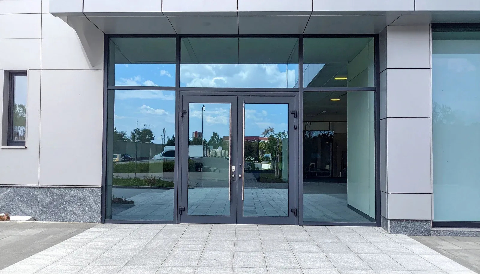 Modern commercial building entrance displays double glass doors within dark metal framing, surrounde 