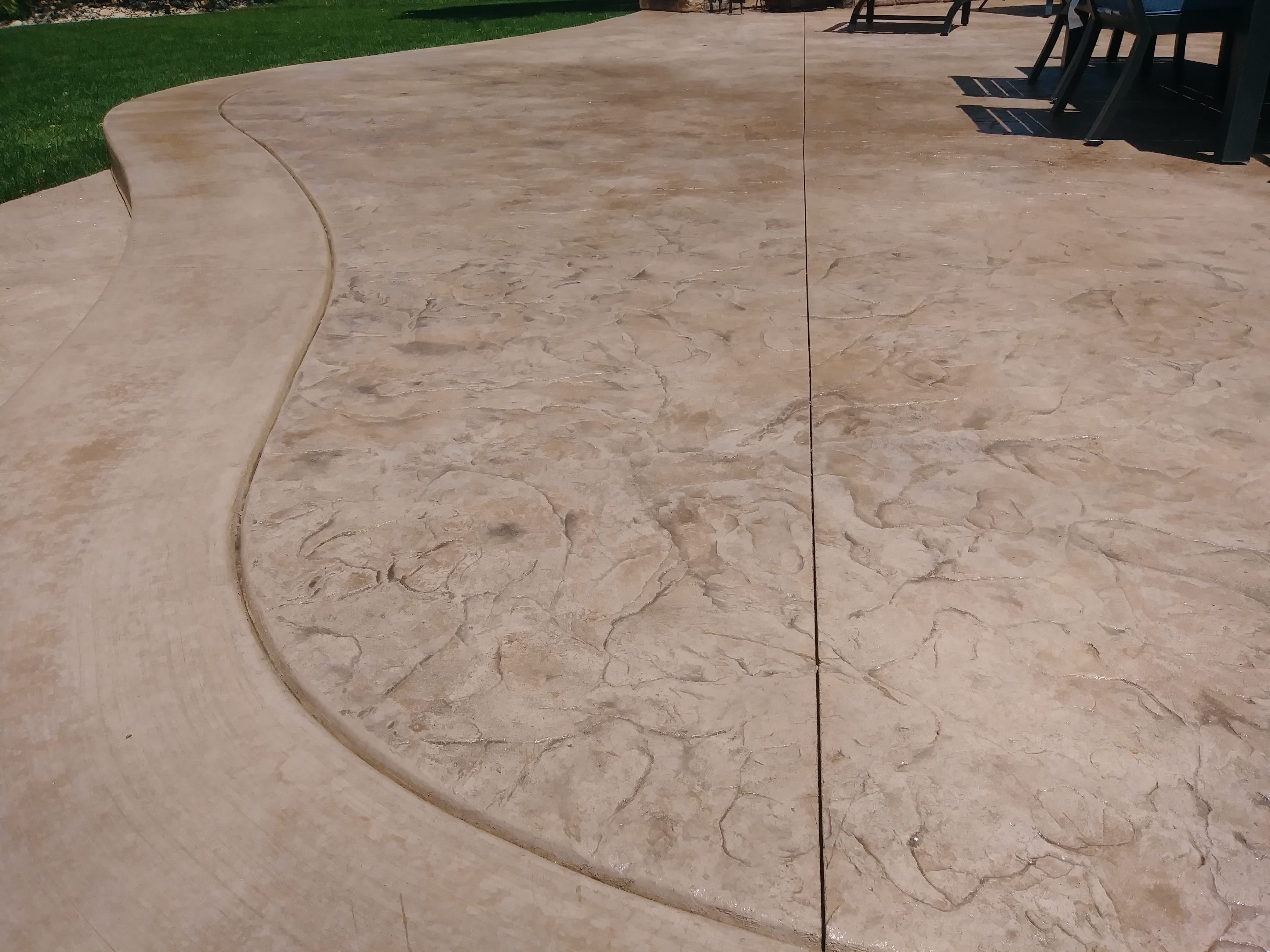 Decorative stamped concrete patio with a natural stone texture and warm earth-tone coloring, creating an attractive outdoor entertaining space.