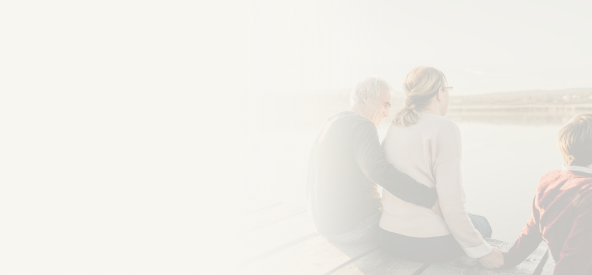 A couple and child sitting on a dock and looking out at the lake.
