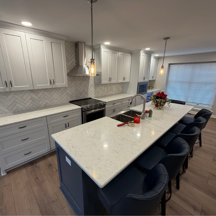 This custom kitchen remodel by Fee Construction LLC in Evansville, IN features gray shaker cabinets, a herringbone tile backsplash, quartz countertops, a navy island with bar seating, and industrial pendant lighting. Fee Construction creates beautiful, functional kitchens tailored to your vision. Call (812) 626-1013 or visit feeconstruction.com to start your kitchen renovation today.