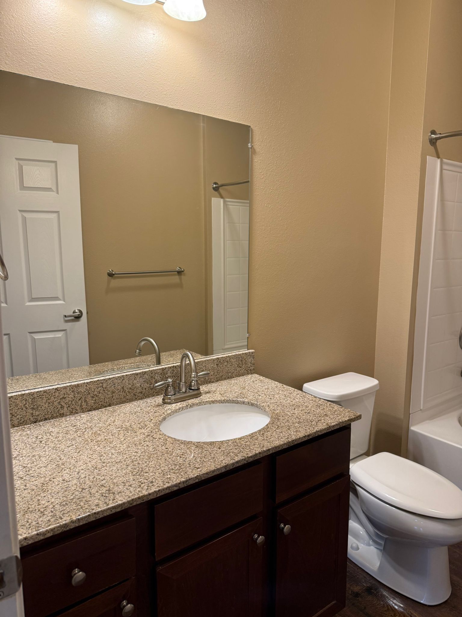 Bathroom interior with granite countertop vanity, white sink, and chrome faucet. A large mirror, toilet, and bathtub with shower are visible, creating a clean and practical residential bathroom layout.