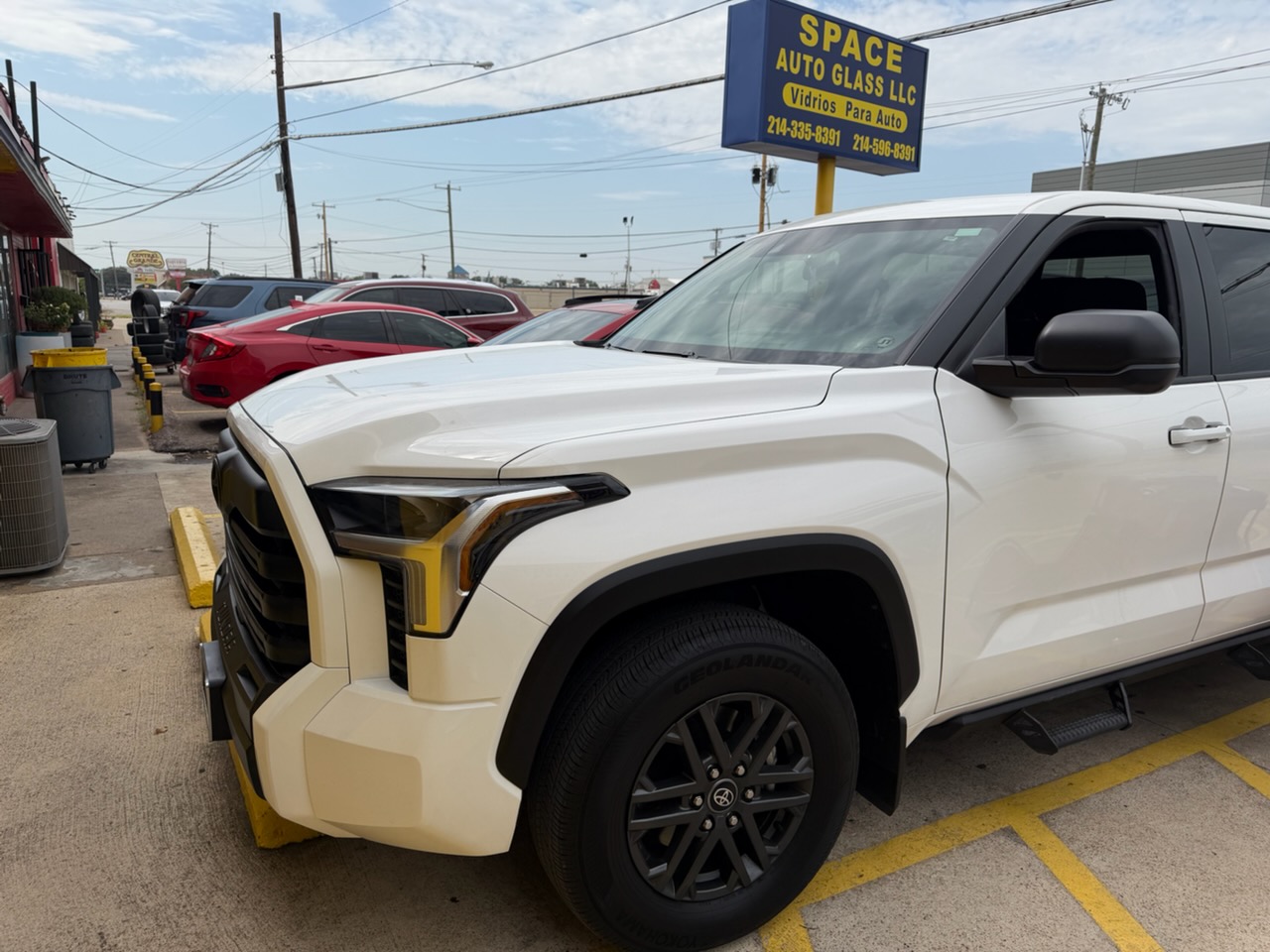 A white Toyota truck parked outside the Space Auto Glass shop, with the business sign visible in the background. The image showcases professional auto glass service for trucks and SUVs.