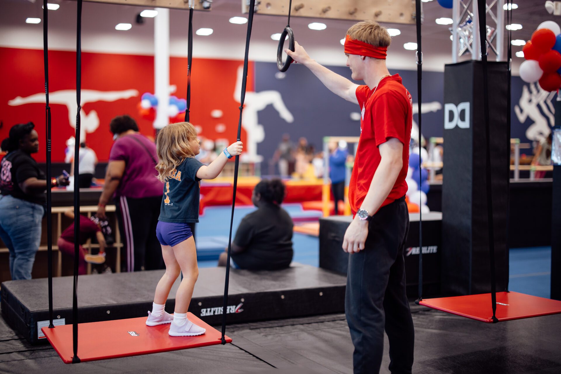 Gymnastics coach helping a young gymnast with a junior ninja training course
