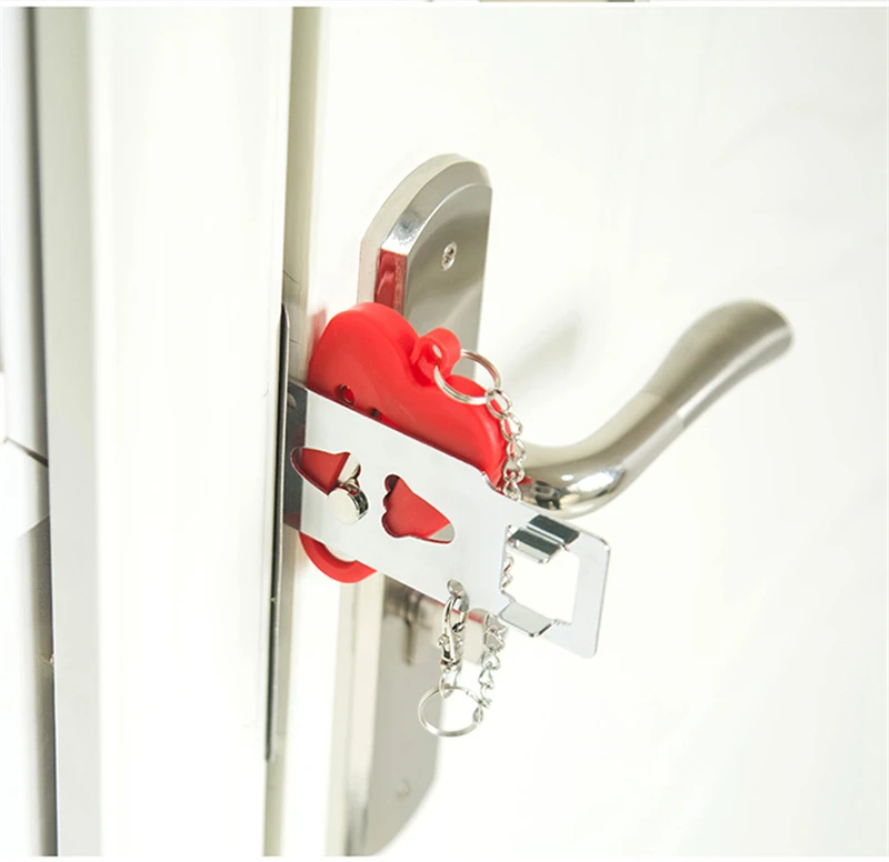 A red heart-shaped lock and two keychains hang from a silver door handle against a white door.
