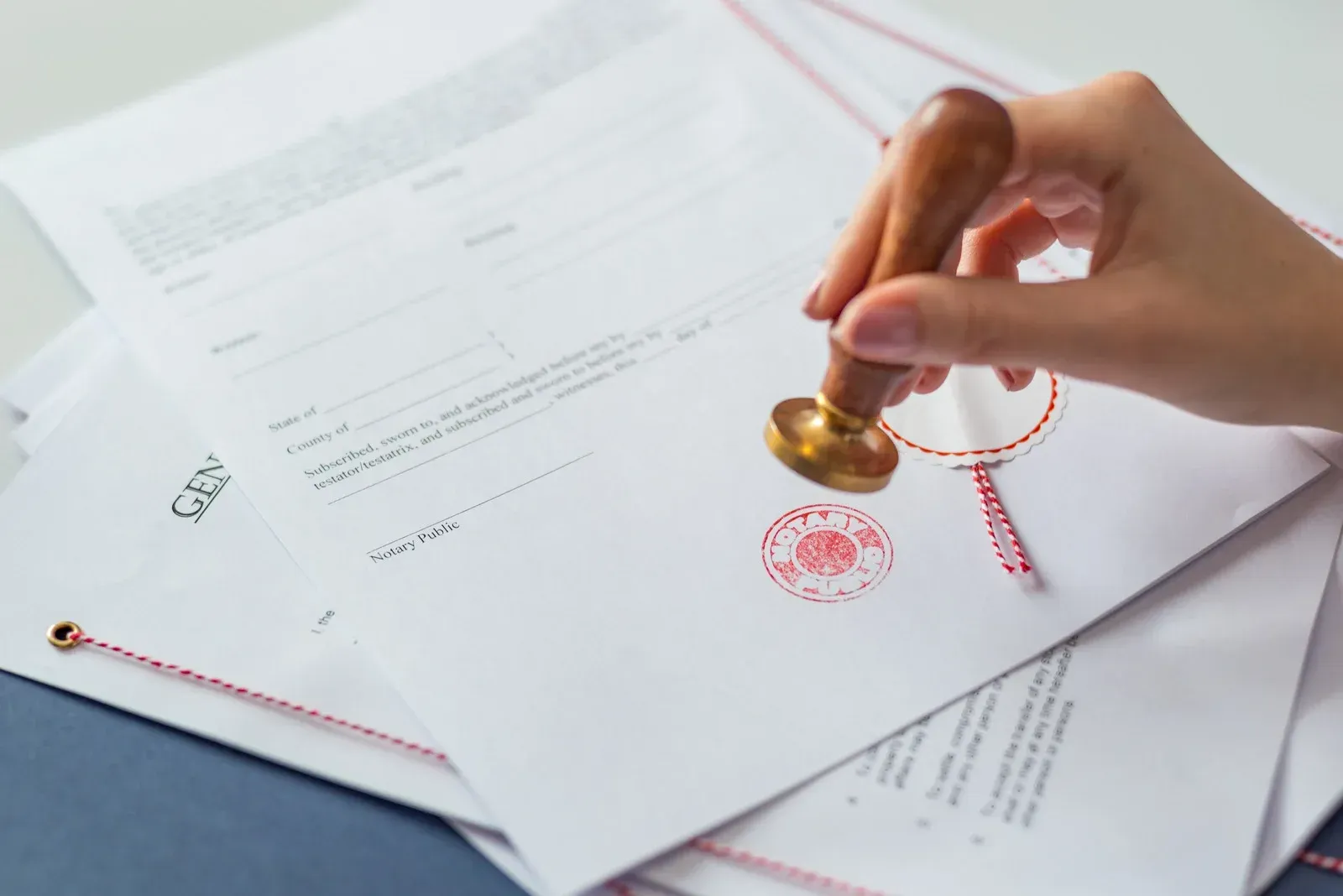 Close-up of hand stamping official document with seal, highlighting notarization process, authentication, legal validation, and formal approval of paperwork required for contracts, agreements, and real estate closing transactions.
