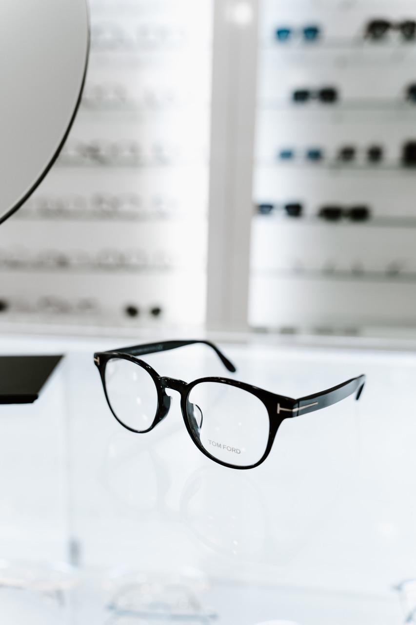 Black Tom Ford eyeglass frames displayed on a glass counter inside TK Optometry in Brooklyn, NY. 