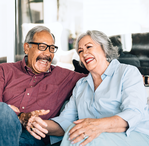 An elderly couple laughing together on the couch.