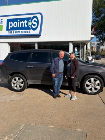 Two happy Walker Tire Point S customers standing beside their SUV outside our automotive service center.