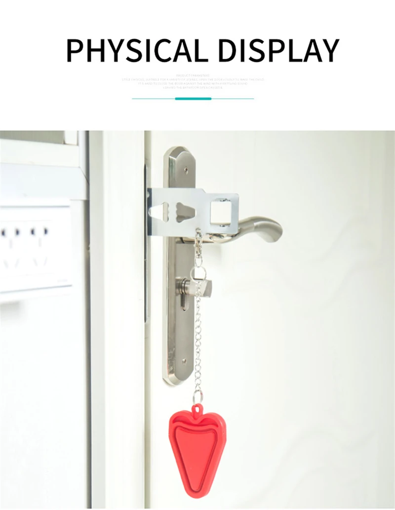 A red heart-shaped object hangs from a door handle by a chain. The object appears to be made of plastic and has a smooth, glossy finish. The door handle is made of silver-colored metal and is attached to a white door. The background is a plain white wall.