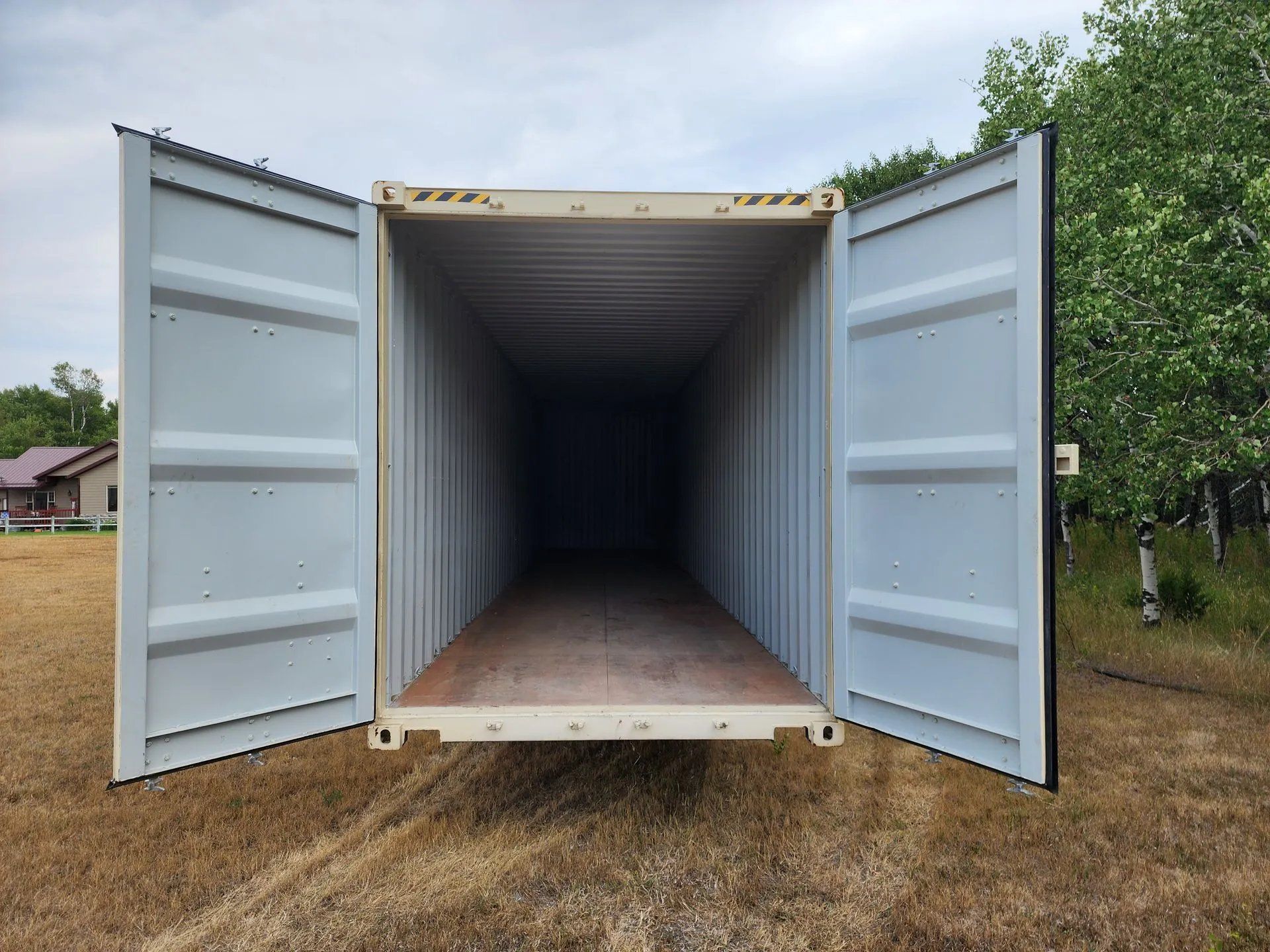 Open portable storage container placed on grassy land with both doors wide open, showing spacious interior used for secure storage, moving, and onsite storage solutions for residential or commercial use.