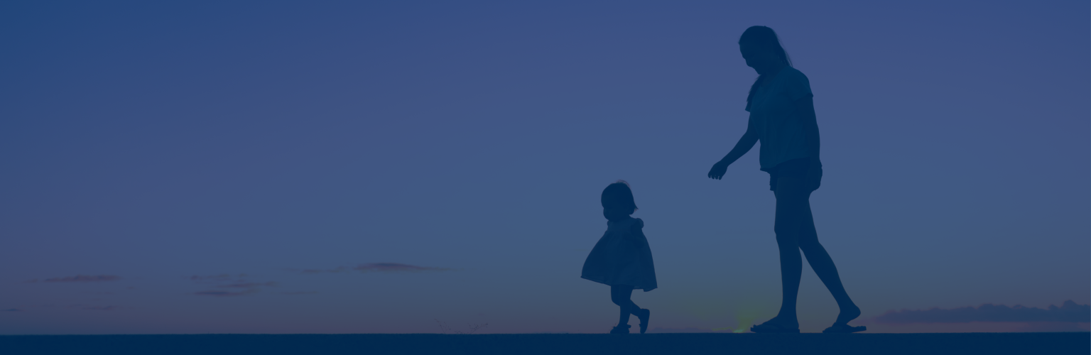 Silhouettes of a woman and baby out for a walk together at sunset.