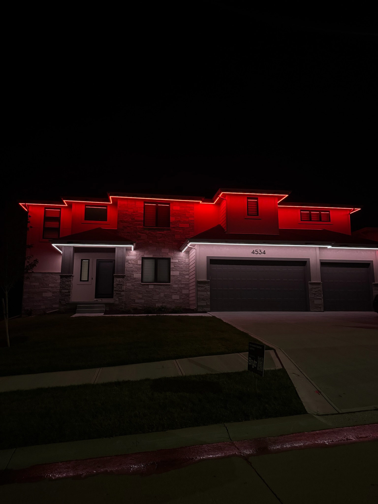 Red architectural lighting illuminating the roofline and exterior of a residential property at night.
