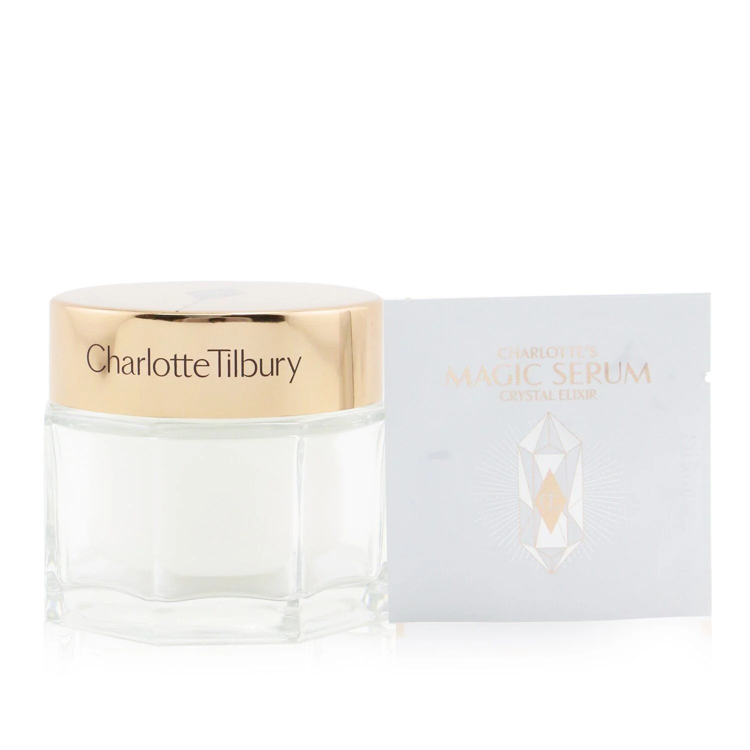 A Charlotte Tilbury Magic Serum Crystal Elixir sample packet is next to a jar of cream with a gold lid that also says Charlotte Tilbury.