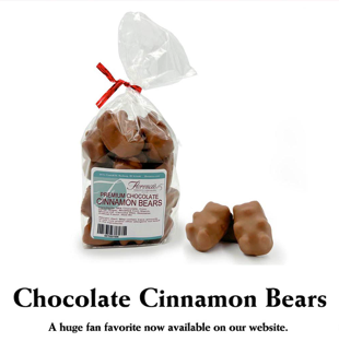 This photograph features a bag of Florence's Exquisite Chocolates' "Premium Chocolate Cinnamon Bears," likely from their Rexburg, Idaho location. The clear bag allows the chocolate-covered cinnamon bears to be clearly seen, tied with a festive red ribbon. The product label identifies them as "Premium Chocolate Cinnamon Bears" and includes a barcode. Several loose chocolate-covered cinnamon bears are scattered beside the bag, revealing their detailed bear shape and milk chocolate coating.