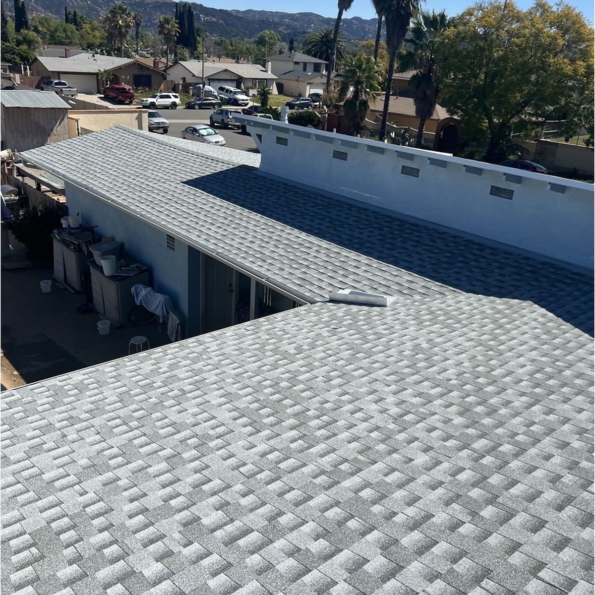 High-angle shot of a multi-level residential building featuring light gray architectural asphalt shingles, modern roof structures, and a clear view of the surrounding neighborhood.