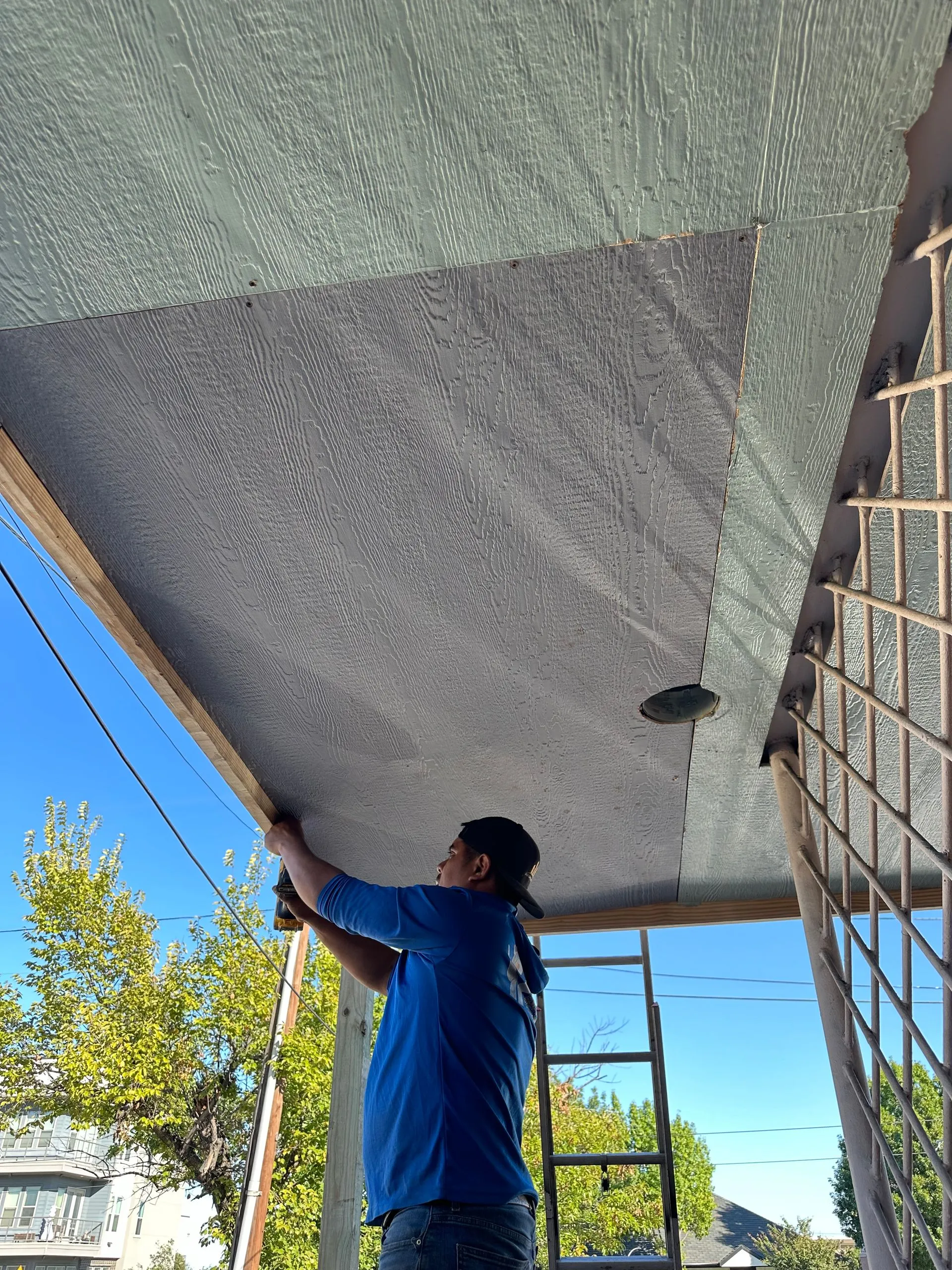 Contractor carefully installs exterior soffit panels beneath a residential roof overhang, improving  