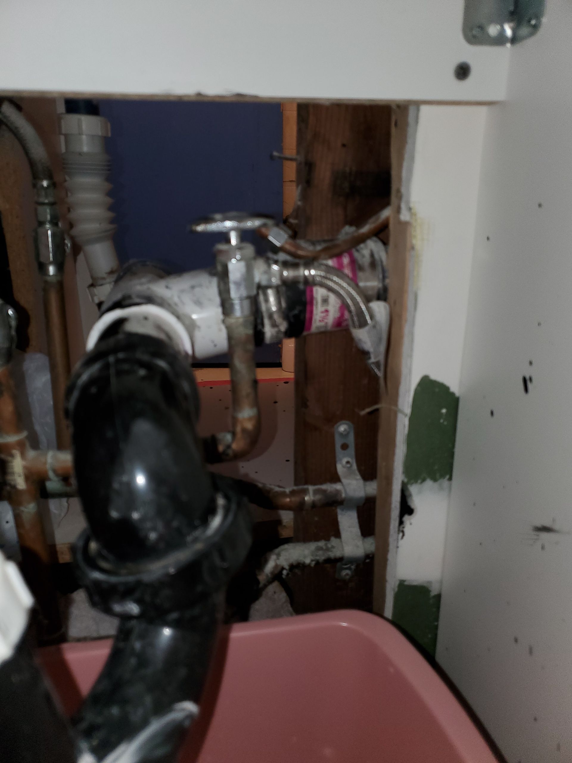 Under-sink plumbing setup with visible pipes, valves, and connections, showing signs of wear, corrosion, and potential leaks, highlighting need for inspection, repair, and proper maintenance of household plumbing system.