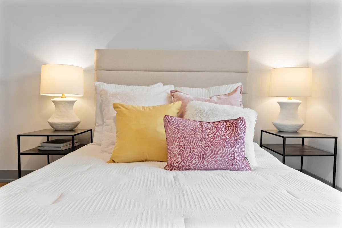 A bed with a white comforter and two pillows with a pink and yellow pillow. 