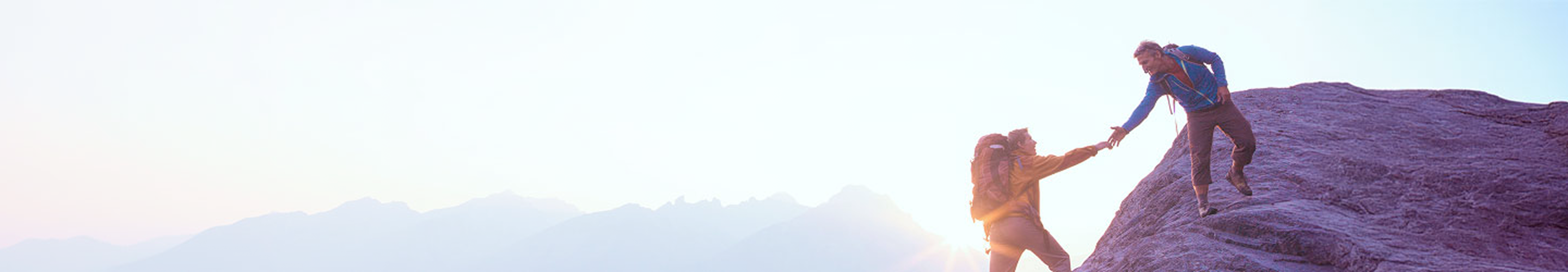 A person lending a helping hand to another person on a mountain hike.