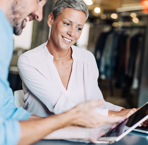 A short-haired woman talking to her financial advisor and looking down at his tablet.