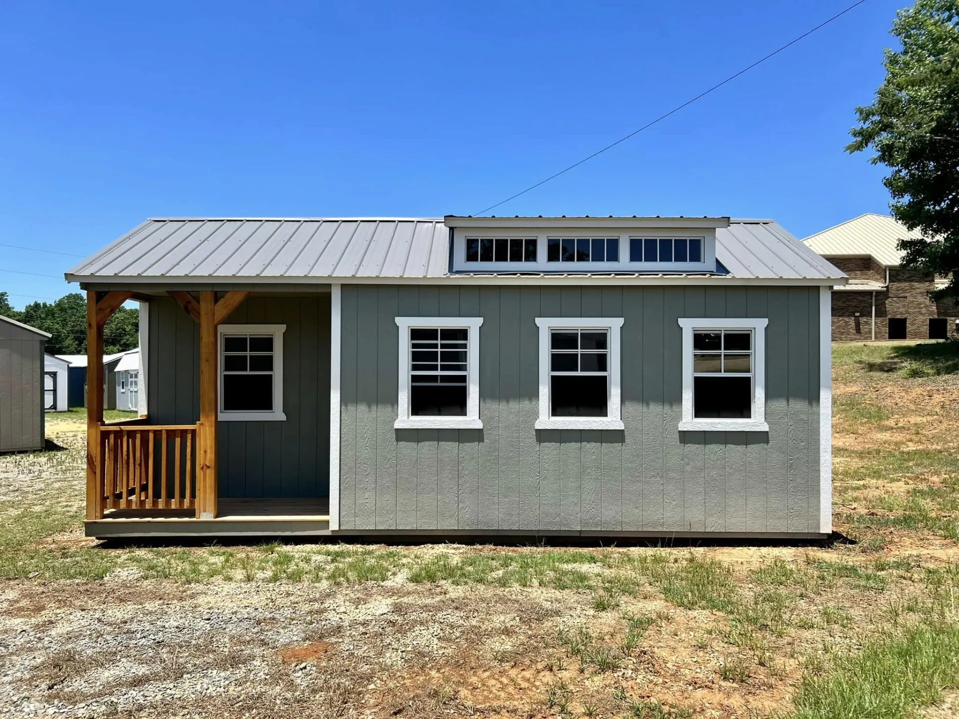 Gray portable building featuring covered porch, clerestory windows, white trim, and multiple side windows. Constructed with durable materials for long-lasting residential, office, or recreational applications.