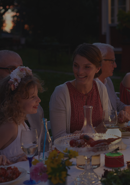 A woman looking lovingly at a child during a multigenerational family dinner outside.