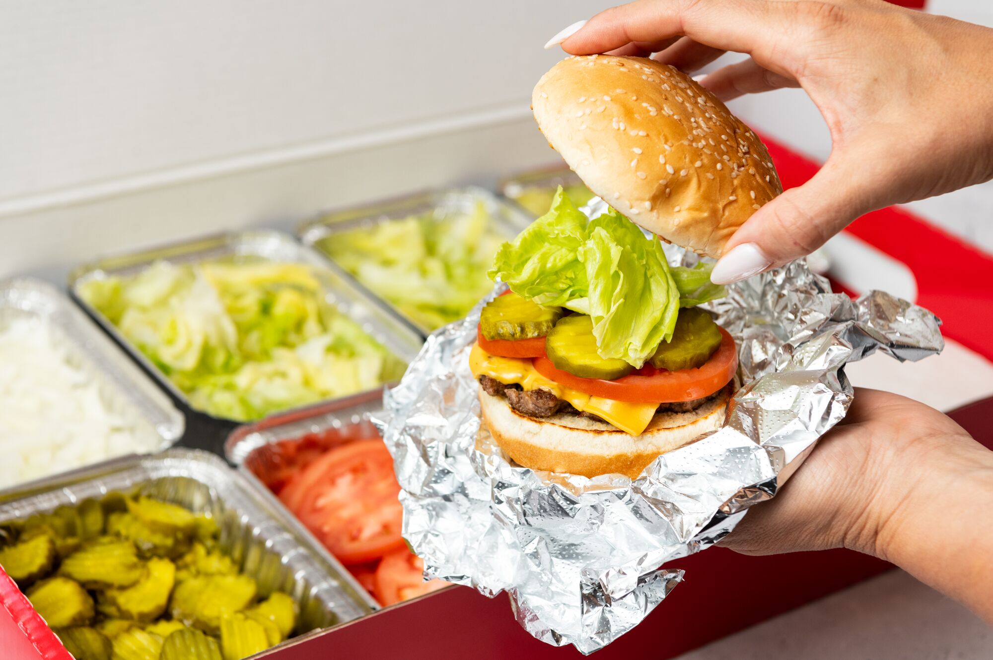 A close-up photo of a person putting the top bun of their cheeseburger in front of a Five Guys cater Five Guys Thousand Oaks (805)496-0173