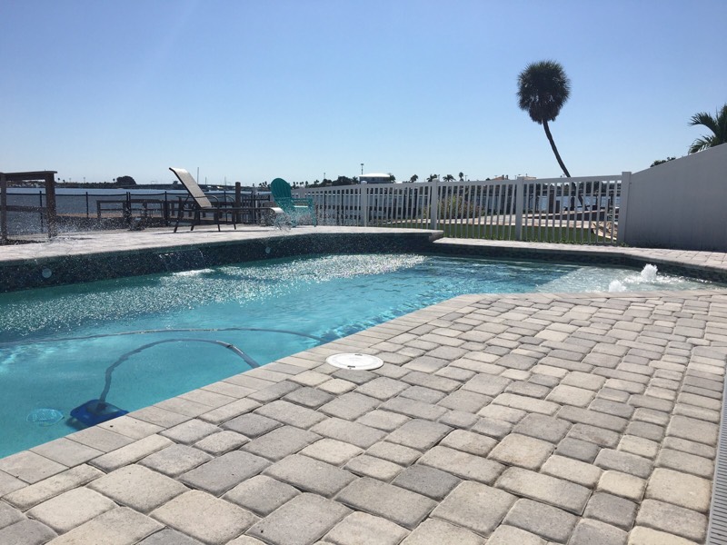 Waterfront swimming pool with expansive paver decking and open views beyond the pool area.